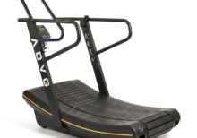 ADVG CurveMax commercial curved manual treadmill, all-black with yellow accent stripe, front three-quarter studio view